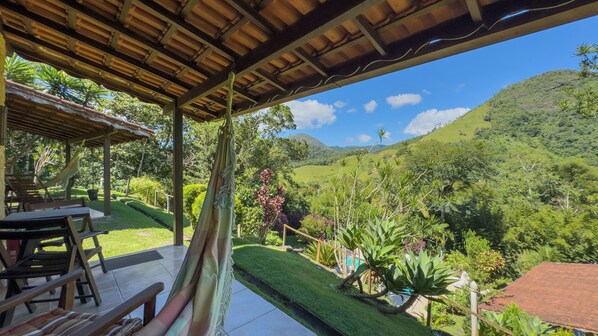 A covered outdoor seating area with a view of a lush valley and hills. - Pousada Jardim Real (Nova Friburgo)