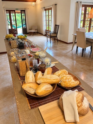 Ein reichhaltiges Buffet mit verschiedenen Speisen und Brot auf einem langen Tisch in einem Raum mit großen Fenstern und Blick auf Grünflächen.