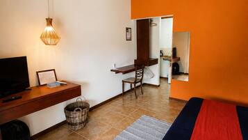 A bedroom with a bed, a desk, a chair, a television, and a hanging light fixture.