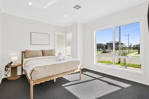 A bedroom with a large window, a bed with a wooden frame, and a nightstand with a lamp. - Coastal Haven at Charlemont (Charlemont)
