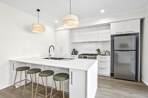 A modern kitchen with white cabinetry, a stainless steel refrigerator, a gas stove, and two pendant lights. - Coastal Haven at Charlemont (Charlemont)