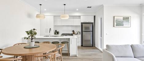 A modern kitchen with white cabinets, a stainless steel refrigerator, and pendant lighting.