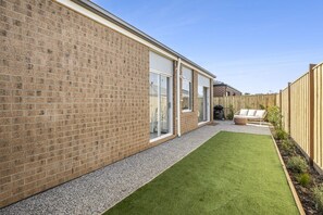 Ein wohnlicher Hinterhof mit einer Ziegelmauer, einem Rasen, einer Terrasse mit Gartenmöbeln und einem Holzzaun.