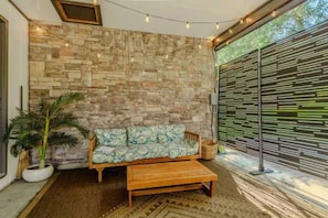 A room with a stone wall, a wooden bench, a patterned sofa, and a large window with a view. - Vantara Smoky Views - Feels like home (Sevierville)