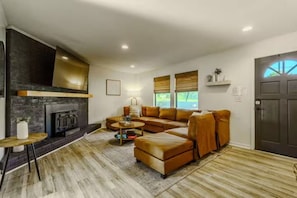 A modern living room with a fireplace, leather sofa, and a dining area with a small table. - Vantara Smoky Views - Feels like home (Sevierville)