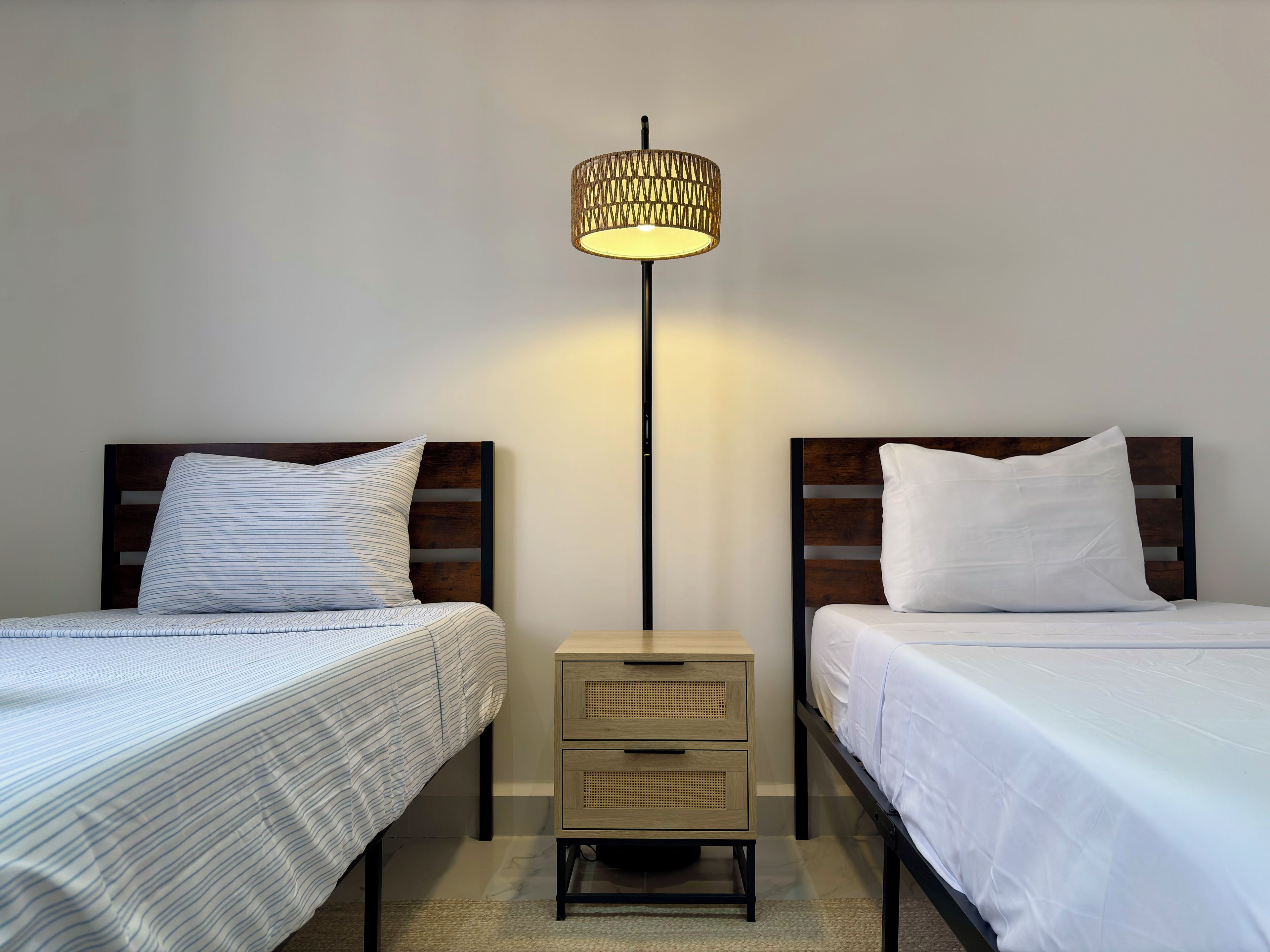 Une chambre à coucher avec deux lits, chacun doté d’une tête de lit en bois, d’une table de chevet avec des tiroirs et d’une lampe de sol.