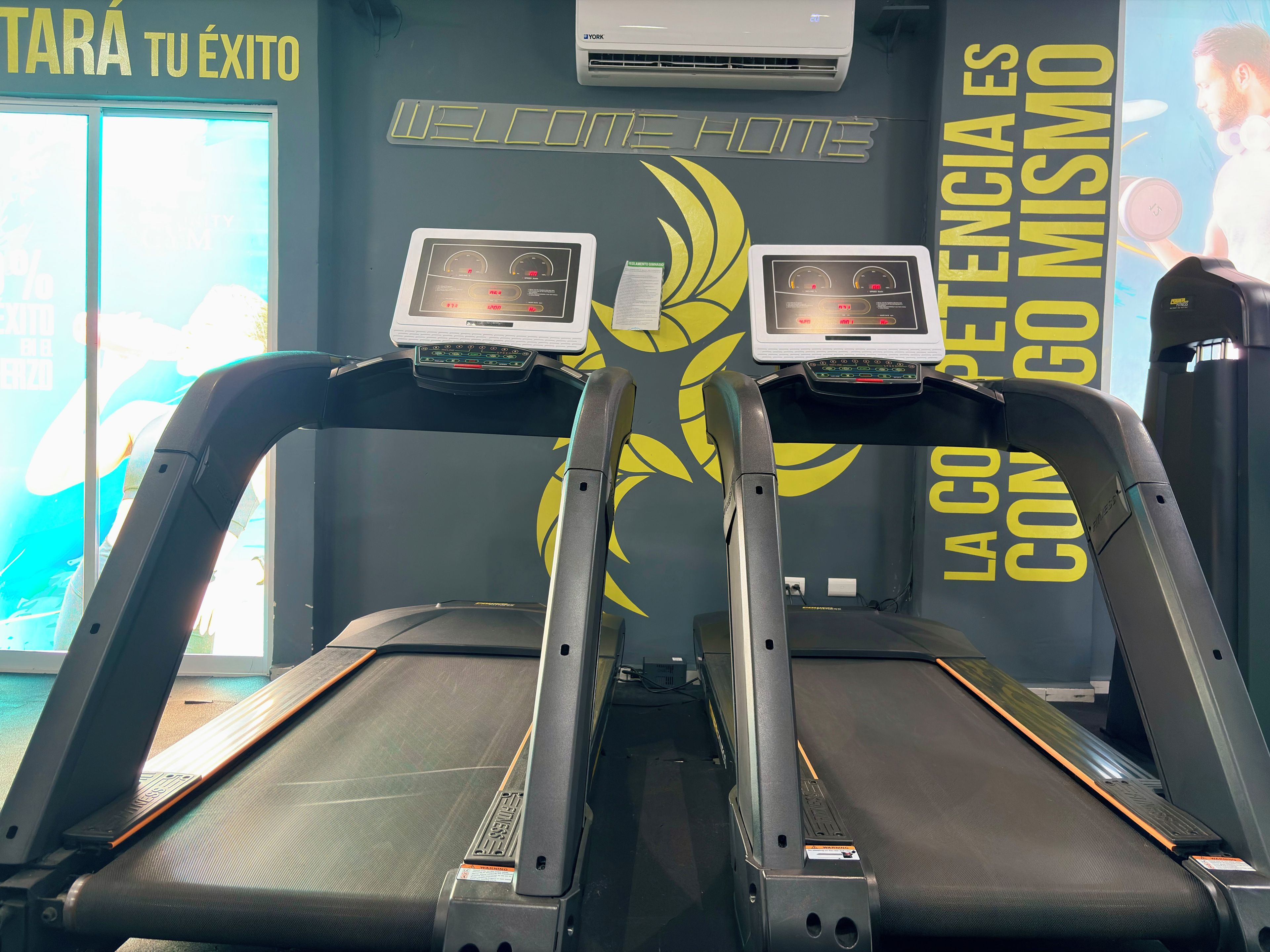 A gym with treadmills, a wall with motivational text, and an air conditioning unit.