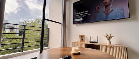 A modern living room with a large TV mounted on the wall, a round wooden table with a remote control, a decorative vase, and a framed picture on a wooden console.
