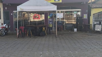 Edifici de dues plantes amb un rètol de restaurant, una zona d'estar a l'exterior coberta i una moto aparcada a fora.