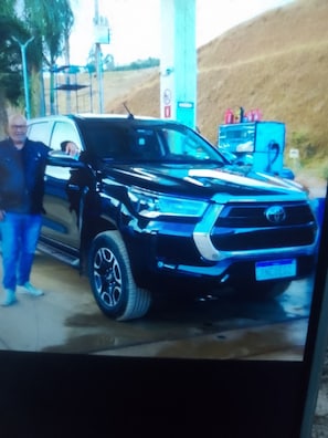 Un SUV negre estacionat a una benzinera, amb una vàlvula de combustible visible i una persona al seu costat.