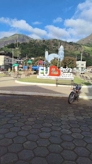 A paved area with hexagonal tiles, a sign with 'EU Pedra Bonita' and a cross, and a mountain in the background.