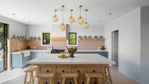 A modern kitchen with a large island, pendant lights, and a view of the outdoors. - The Distiller's Retreat (Takaka)