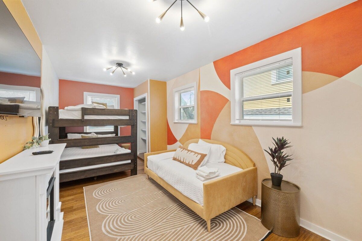 Une chambre avec des lits superposés, une table de chevet, une lampe et une fenêtre avec des stores.