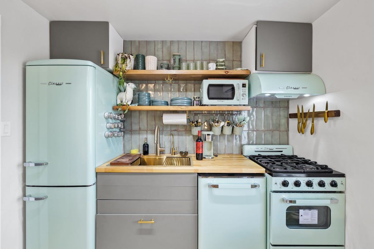 Cozinha compacta com estética vintage, equipada com geladeira, micro-ondas, fogão e pia com bancadas de madeira.