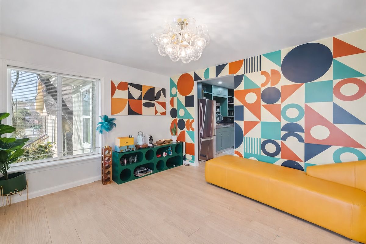 Uma sala de estar moderna com um sofá amarelo, um rack verde e uma parede com padrão geométrico.