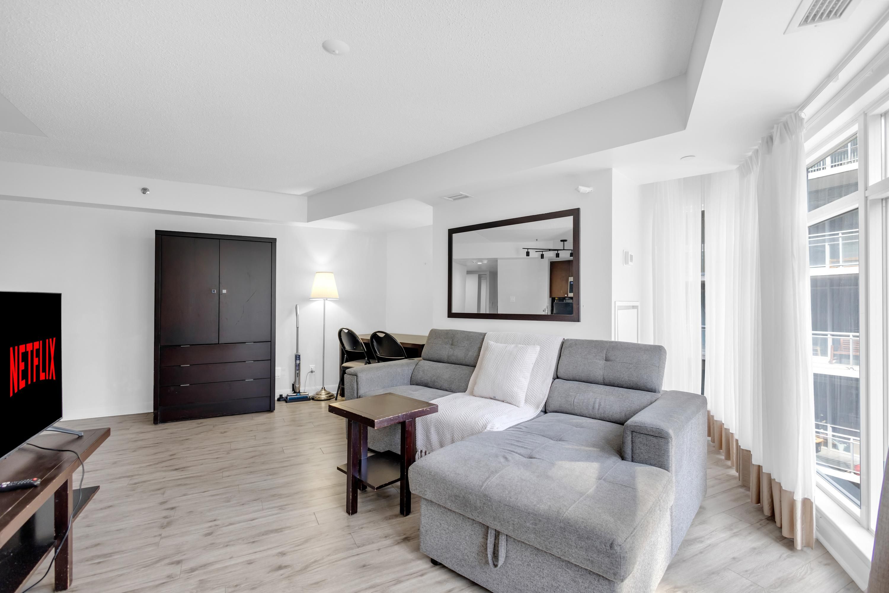 A modern living room with a grey sofa, a small wooden table, a TV, and a dark wardrobe.