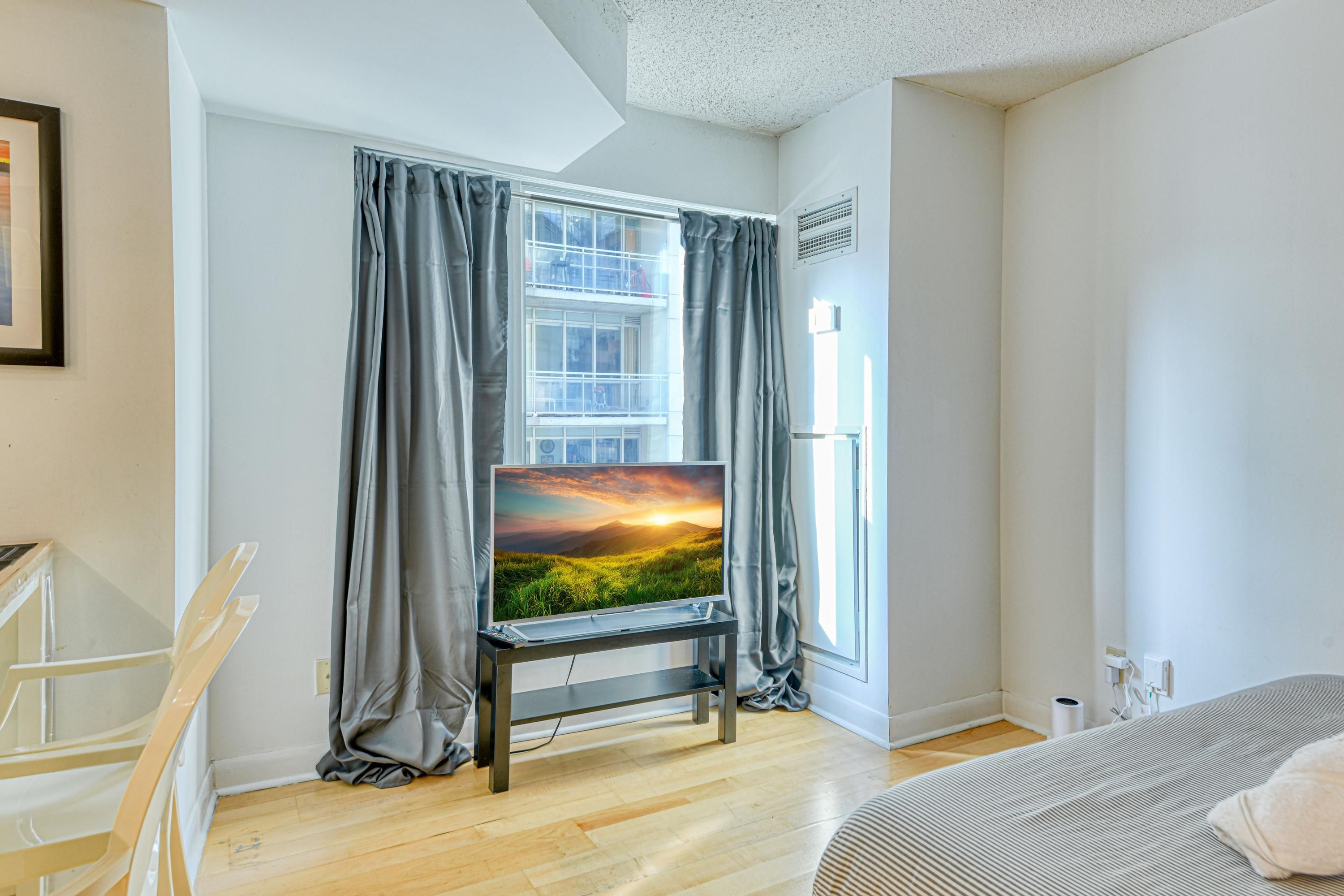 Een moderne kamer met een groot raam, een flatscreen televisie op een standaard, een bed en een stoel.