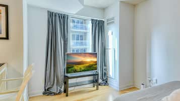 Een moderne kamer met een groot raam, een flatscreen televisie op een standaard, een bed en een stoel.