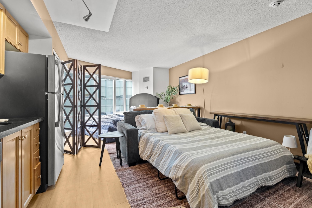 Ein kleines Schlafzimmer mit Bett, Nachttisch, Lampe und Blick ins Freie.