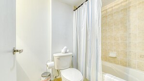 Casa de banho com sanita, um contentor de lixo e cortina de chuveiro.