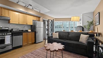 A modern kitchen with wooden cabinets, stainless steel appliances, and a dining area with a dark sofa and a unique coffee table.