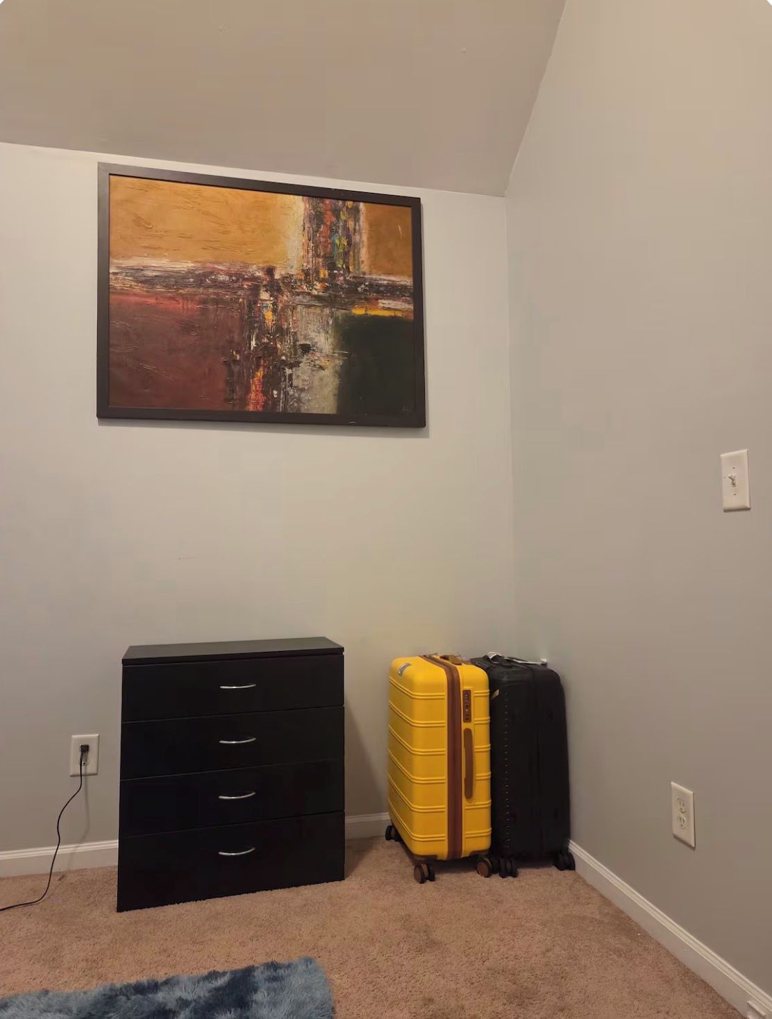 A room with a black dresser, a yellow suitcase, and a painting on the wall.