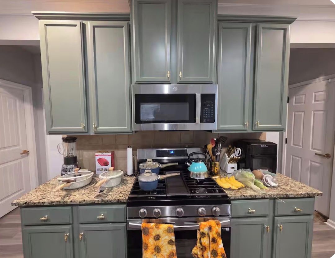 A kitchen with green cabinets, a microwave, a stove, and various kitchen items on the counter.
