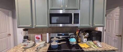 Une cuisine avec des meubles de rangement verts, un four à micro-ondes, une cuisinière et divers ustensiles de cuisine disposés sur le plan de travail.