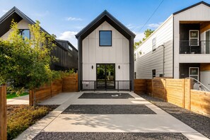 En modern bostadsbyggnad med en central entré, en täckt veranda och en uppfart med grind.