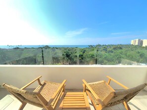 A balcony with two wicker chairs and a wooden table, overlooking a tropical landscape with dense greenery and a clear blue sky. - Spacious 3-bedroom Ocean View apartment Flamingos Nuevo Vallarta (Nuevo Vallarta)