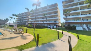 A multi-story hotel with a pool area, palm trees, and a clear sky. - Spacious 3-bedroom Ocean View apartment Flamingos Nuevo Vallarta (Nuevo Vallarta)