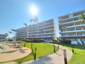 A multi-story hotel with a pool area, palm trees, and a clear sky. - Spacious 3-bedroom Ocean View apartment Flamingos Nuevo Vallarta (Nuevo Vallarta)