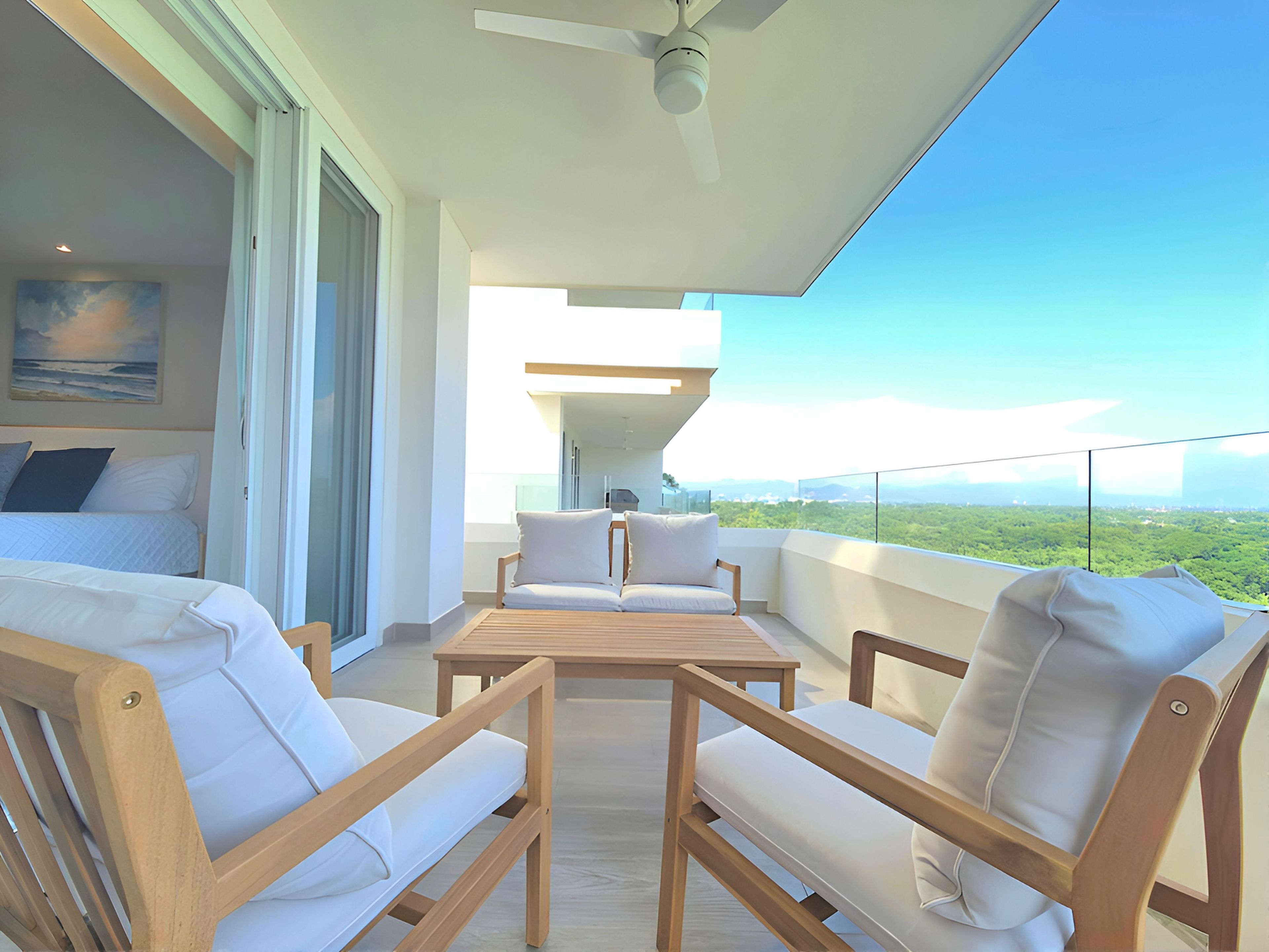 Un balcon avec vue sur le paysage, un lit avec du linge de lit blanc et un ventilateur de plafond.