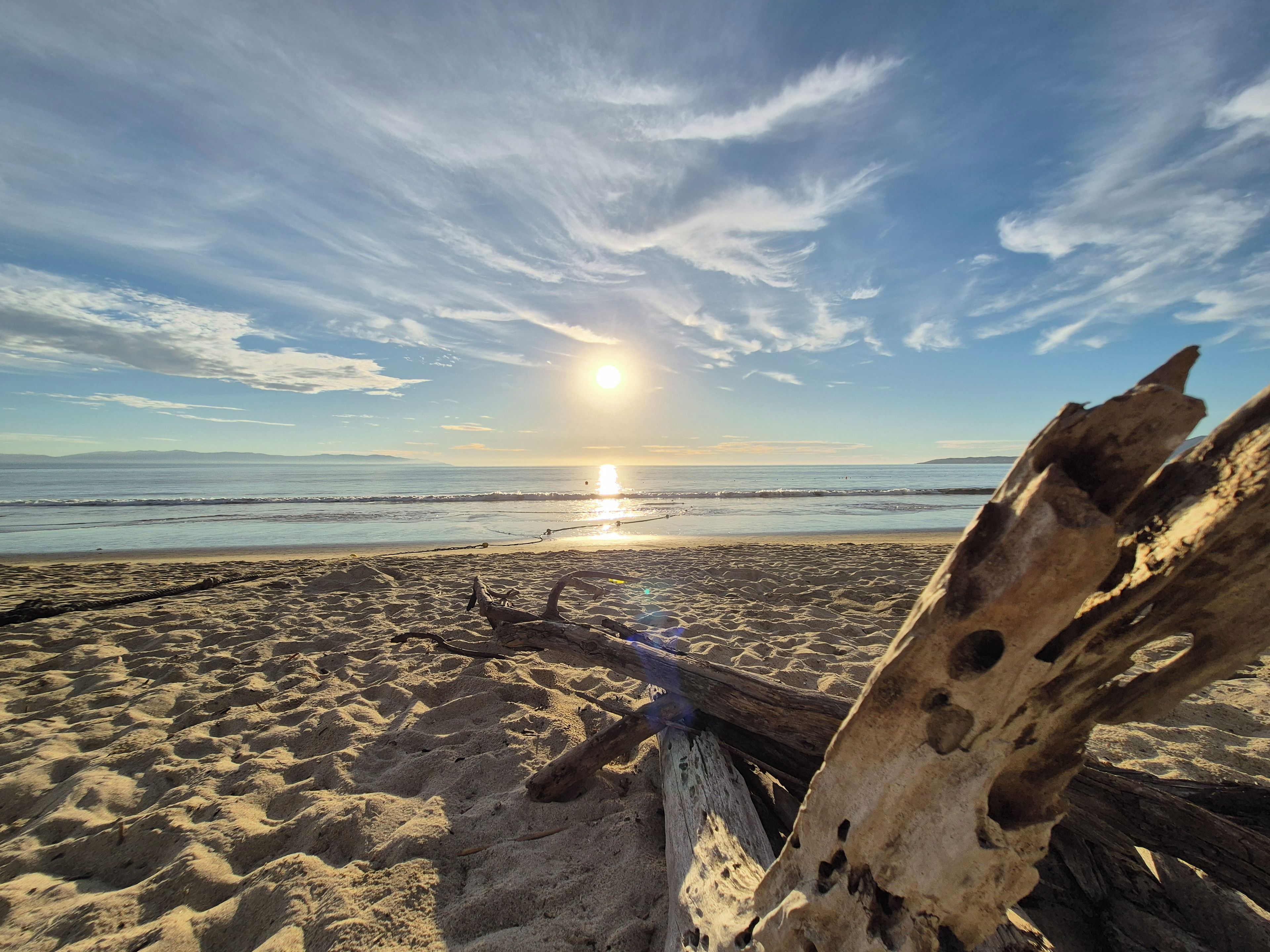A beach scene with a wooden structure in the foreground and a clear sky with the sun setting in the background.