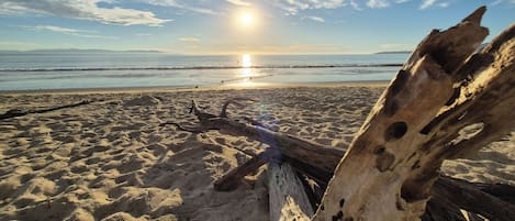 A beach scene with a wooden structure in the foreground and a clear sky with the sun setting in the background.