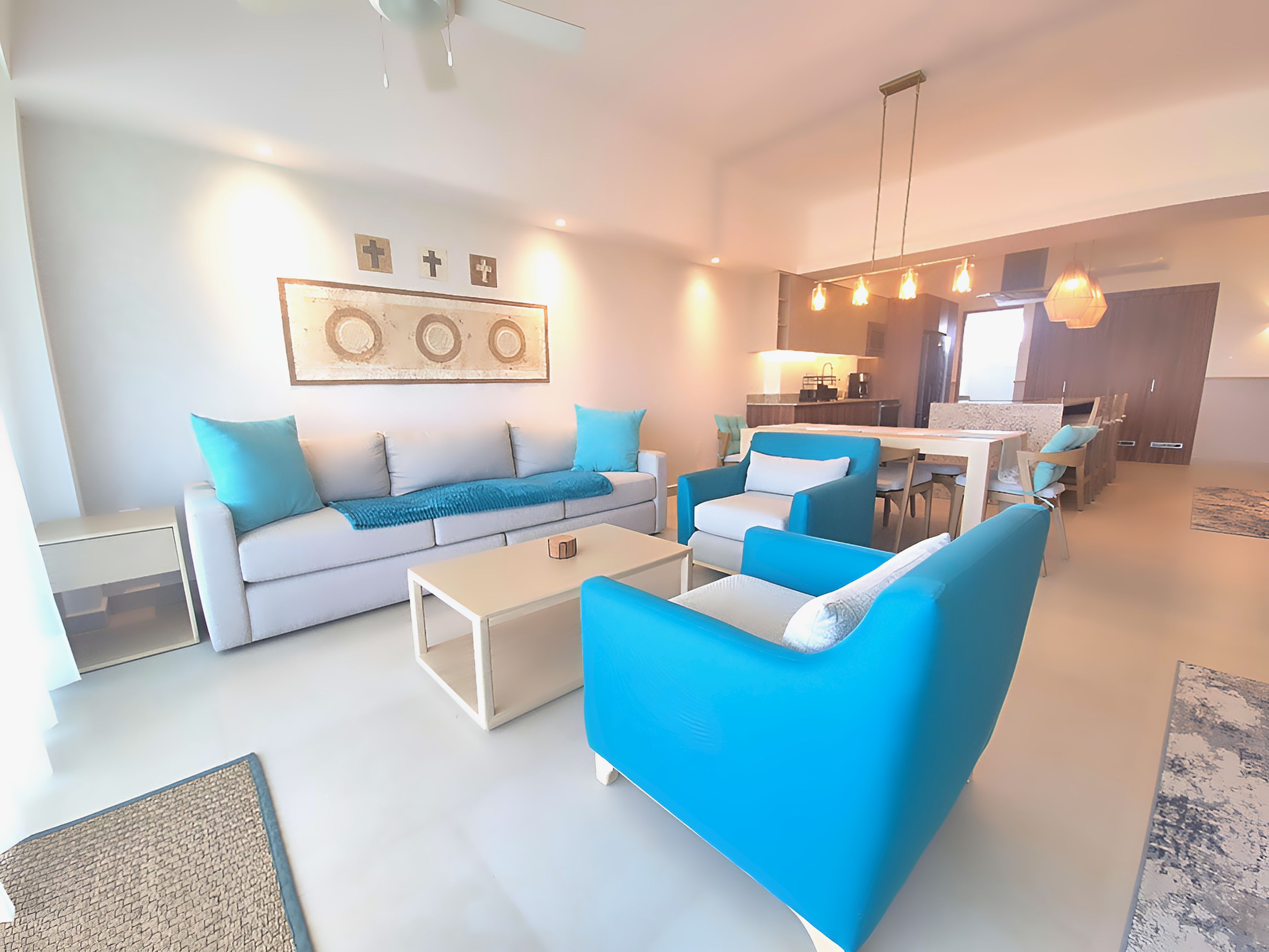 Ein modernes Wohnzimmer mit einer Couch, Sesseln und einem Couchtisch. Es gibt eine Küchenzeile mit einem Esstisch und Stühlen.