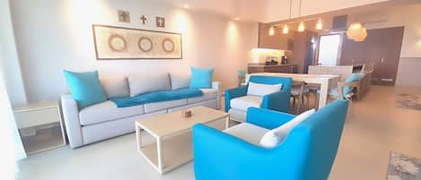 Una sala moderna con un sofá, sillones y una mesa de centro. Cuenta con una zona de cocina con una mesa y sillas para comer.