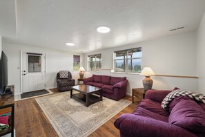 Ein Wohnzimmer mit Sofa, Sessel und Couchtisch, einer Tür und einem Fenster mit schöner Aussicht.
