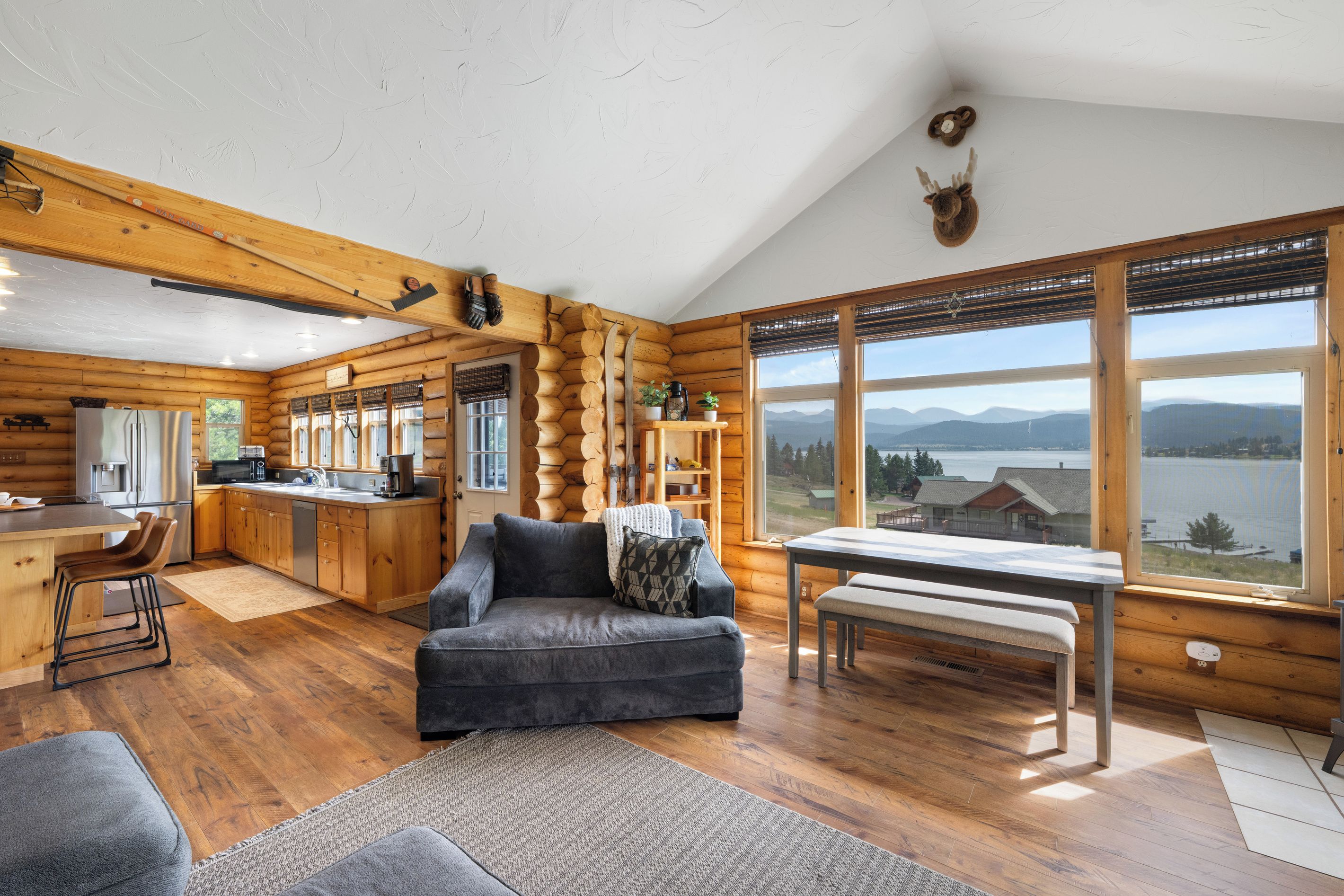L’intérieur d’une cabane en rondins comprend une cuisine, un coin repas et une grande fenêtre donnant sur les montagnes et un lac.