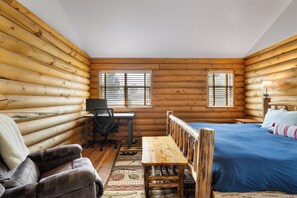 Una habitación tipo cabaña de madera con cama, escritorio, silla y lámpara.
