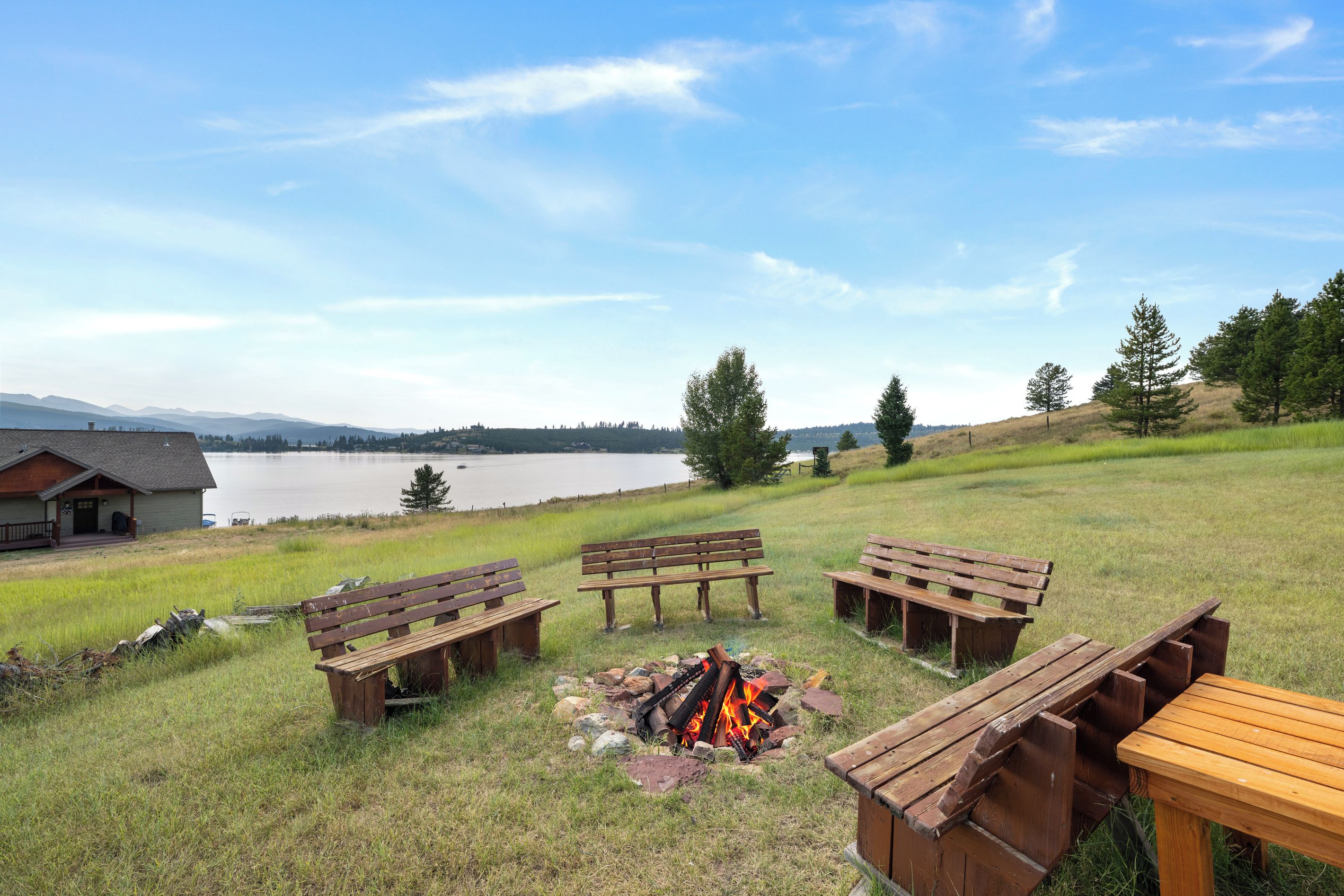 A lakeside outdoor seating area with wooden benches and a fire pit.