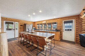 A log cabin interior with a central dining table, bar stools, a kitchen area, and a view through the windows. - Ski Disco, Fish GTL, Philipsburg just minutes away (Anaconda)