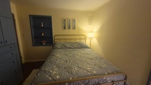 Un dormitorio con una cama, un estante montado en la pared con adornos y una lámpara de noche.