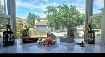 Vista por la ventana con un letrero de bienvenida, una mesita con adornos y dos faroles.