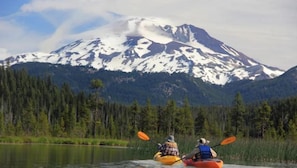 Dos kayakistas en un lago tranquilo, con una montaña nevada al fondo.