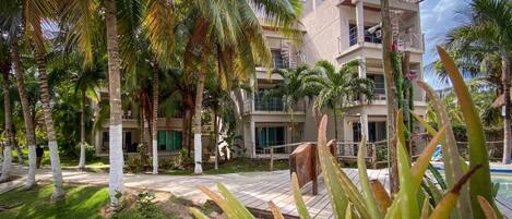 Um resort com área de piscina, palmeiras e um edifício de vários andares com varandas.