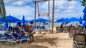 A beach with rows of sun loungers and umbrellas, a wooden swing set, and a sign for 'Chula's Beach Club.'