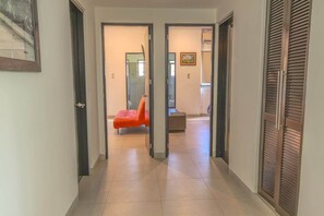 Un couloir avec un sol carrelé, une chaise rouge et une porte en bois sur la droite.