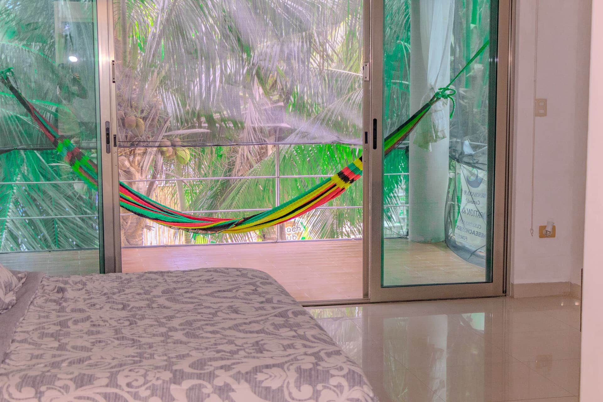 A room with a bed, a hammock, and a view through a glass door.