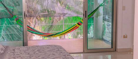 A room with a bed, a hammock, and a view through a glass door.